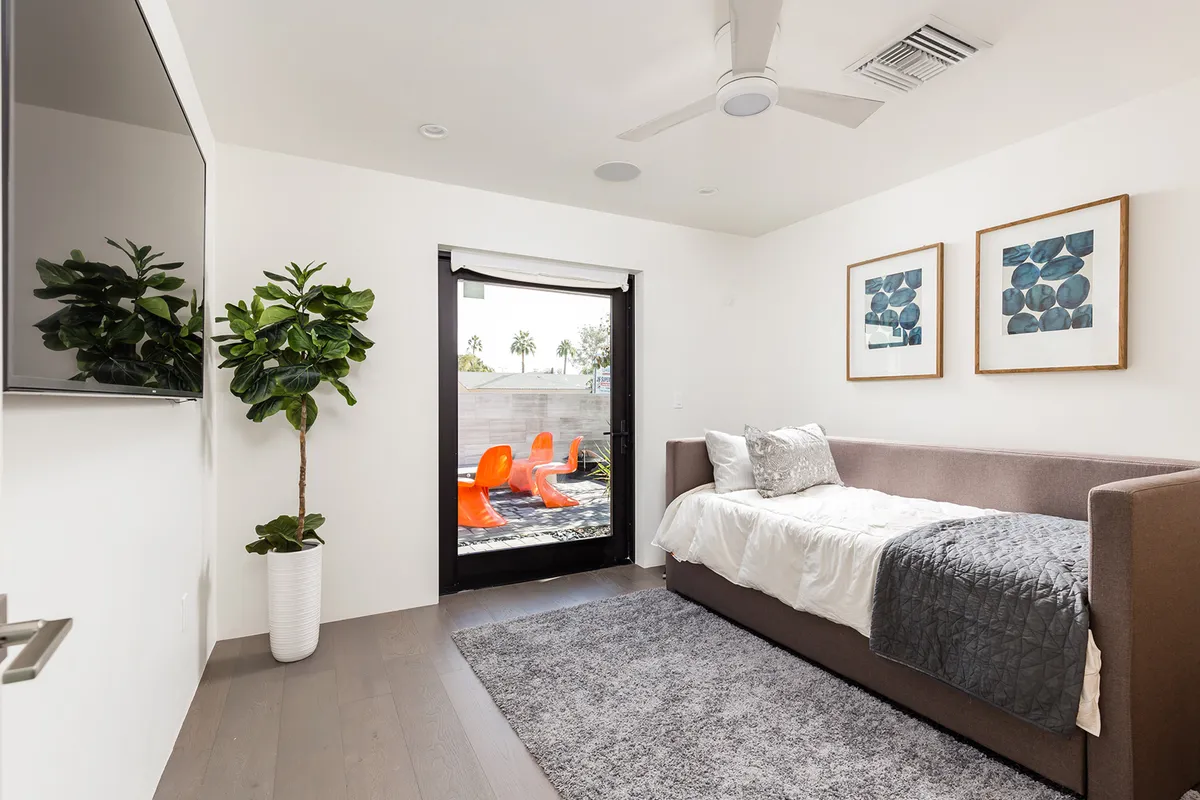 A cozy guest suite with a sofa bed, contemporary artwork, potted plant, and a sliding glass door leading to the outdoors. Sunlight streams through, making it ideal for guests seeking independence and comfort.