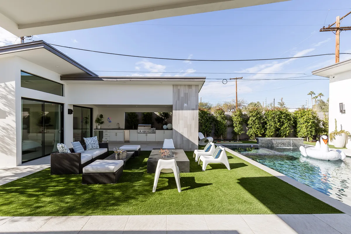 A vibrant backyard scene featuring a sparkling swimming pool, a stylish outdoor seating area, an outdoor kitchen, a lush green lawn, and a whimsical decorative swan float. The setting is perfect for gatherings and relaxation, with ample space to enjoy Arizona's warm sunshine or a cozy evening outdoors.