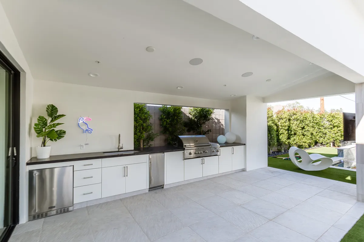 A modern outdoor kitchen with a grill, comfortable seating, greenery, and a decorative neon sign, providing an ideal spot for cooking, entertaining, and relaxed socializing in the fresh air.