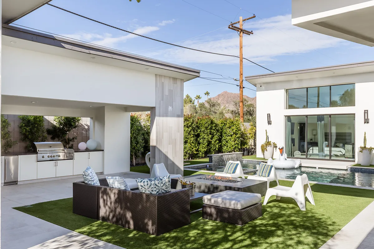 A spacious exterior setup with a swimming pool, outdoor seating area, grill station, and a stunning mountain backdrop. The image conveys a relaxed and cheerful atmosphere, perfect for sunset pool parties and group gatherings by the water.