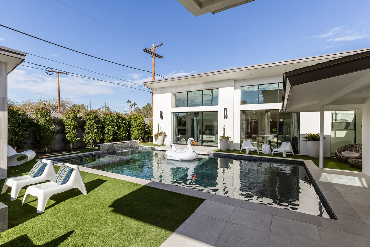 A spacious, sunlit backyard scene showcases a sparkling swimming pool with a playful swan float, modern outdoor seating, greenery, and sleek architectural lines. The area exudes fun and relaxation for all ages.