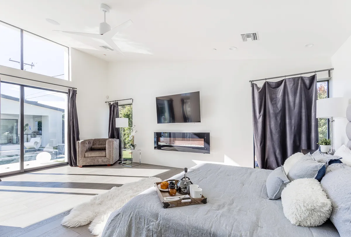 A spacious guest bedroom featuring a large bed with soft bedding, a comfortable armchair for reading or relaxing, and a TV mounted on the wall. The room is filled with natural light from large windows, creating a welcoming and tranquil atmosphere ideal for families or groups who need flexible sleeping arrangements.