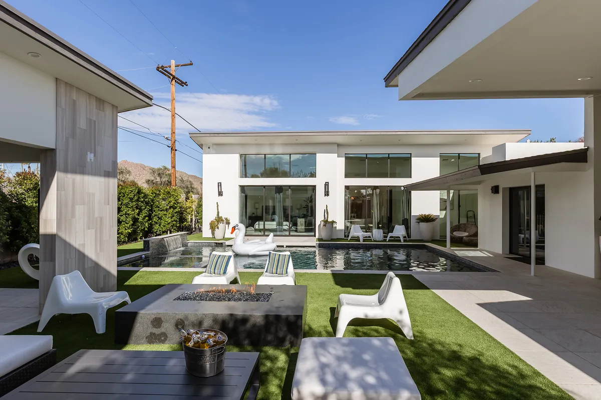 A modern, resort-style backyard oasis featuring a sparkling swimming pool, a cozy fire pit surrounded by lounge chairs, and contemporary architecture. The setting is ready for relaxation or entertaining after a day exploring Scottsdale.