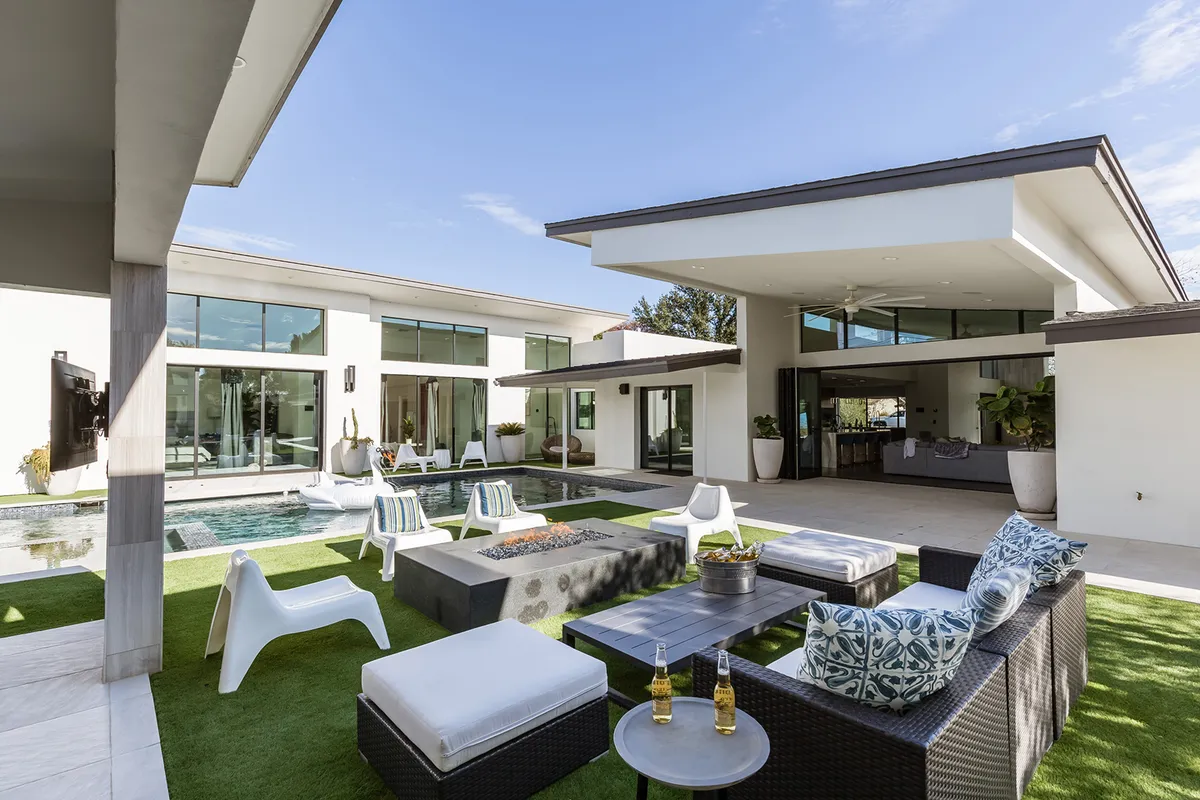 This image features a contemporary outdoor scene with a swimming pool, fire pit, seating area, and an outdoor kitchen. The modern setup invites gatherings, and the fire pit is surrounded by comfortable seating, while the pool glistens nearby. The overall mood is relaxed yet elegant, ideal for group entertainment and leisure.