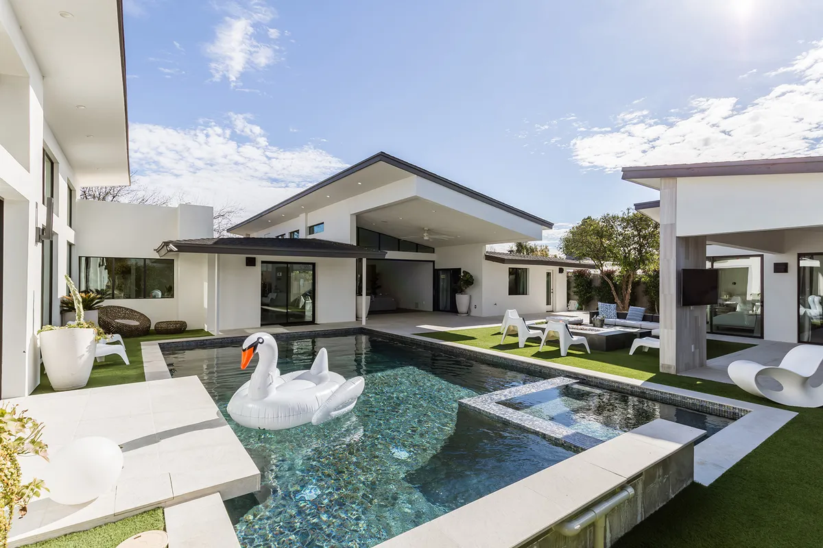The hero image showcases a stunning modern home exterior in Scottsdale, Arizona, centered around a sparkling swimming pool. A whimsical inflatable swan floats in the water, surrounded by inviting outdoor lounge seating and clean-lined architecture. The scene is bathed in warm sunset light, evoking a playful yet luxurious atmosphere ideal for both relaxation and social gatherings.